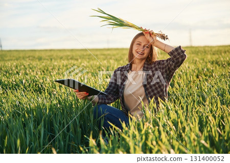 Sitting and smiling. Young woman is on the beautiful agricultural field at daytime 131400052