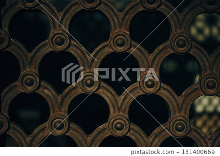 Detailed view of an ornate metal gate with a repeating, circular pattern. Close-up view of an ornate metal gate, showcasing a repeating pattern of circular and arched shapes with a dark background. Detailed view of an ornate metal gate with a repeating, circular pattern. Close-up view of an ornate metal gate, showcasing a repeating pattern of circular and arched shapes with a dark background. 131400669