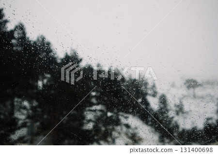 Raindrops on a window create a moody, minimalist scene with trees in the background. Raindrops on a window 131400698