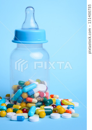 Concept of baby taking pills. Baby`s milk bottle full of pills and capsules against the blue background 131400785