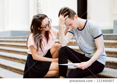 Girl comforting her depressed frustrated friend and gives him some help. Student boy failed exam, holding paper with result and very depressed Girl comforting her depressed frustrated friend and gives him some help. Student boy failed exam, holding paper with result and very depressed 131400807