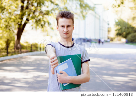 Disappointed university student showing thumbs down is not satisfied with studying in the university because of inexperienced teaching stuff, old technologies, and equipment 131400818