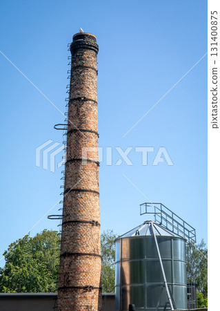 Old Industrial Brick Chimney and Modern Metal Silo Against Clear Blue Sky 131400875
