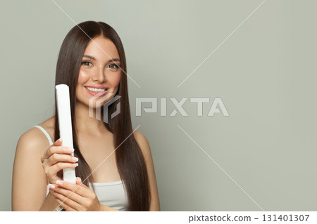Smiling woman brunette with long straight smooth hairstyle using hair straightener iron  131401307