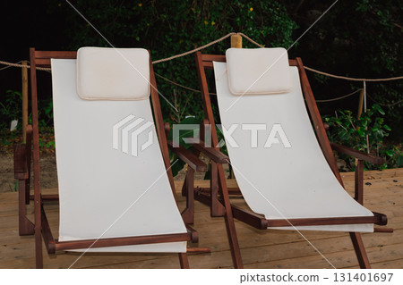 Comfortable lounge chairs with white cushions located in a forest recreation area for enjoying beauty and fresh air Comfortable lounge chairs with white cushions located in a forest recreation area for enjoying beauty and fresh air 131401697