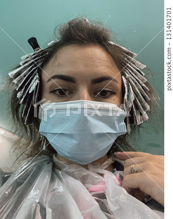 Girl taking a selfie while dyeing her hair with a medical face mask on 131401701