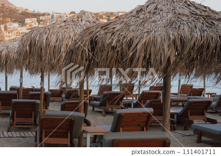 Beach relaxation area with straw umbrellas and sun loungers on sandy shore near the water Beach relaxation area with straw umbrellas and sun loungers on sandy shore near the water 131401711