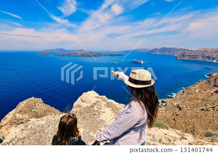 Mother and daughter watching cruise ship and pointing to nearby island, Santorini, Greece 131401744