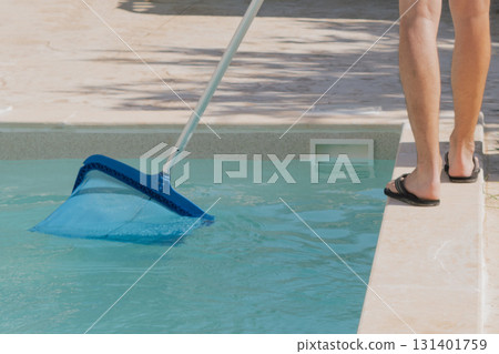 Young man cleaning private swimming pool with a skimmer. Skimmer is used to remove leaves, insects and floating debris from pools 131401759