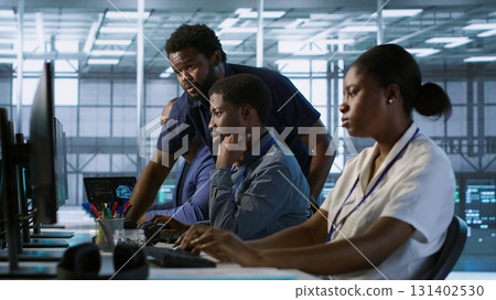Manager supervising server room workers developing disaster recovery plans ensuring minimal downtime. Supervisor oversees data center technicians using data analytics to monitor performance, camera A Manager supervising server room workers developing disaster recovery plans ensuring minimal downtime. Supervisor oversees data center technicians using data analytics to monitor performance, camera A 131402530