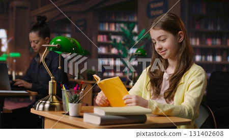 Young teen girl engrossed in reading books at the school library, focusing on literature and knowledge while she is preparing for her academic lessons and other class assignments. Camera B. Young teen girl engrossed in reading books at the school library, focusing on literature and knowledge while she is preparing for her academic lessons and other class assignments. Camera B. 131402608