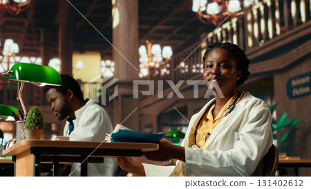 Focused medical student enjoys reading a textbook on pharmacology, preparing for an important med school exam. Woman pupil at the university library learning for her career. Camera B. 131402612