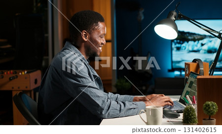 African American freelancer researching data driven topics at his home workstation, planning work schedule and completing project tasks. Managing job from a comfortable setup. Camera B. 131402615