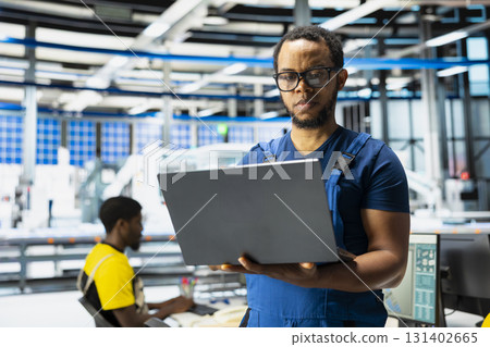 Black supervisor developing power optimization in solar panel production, working on laptop to increase sustainable renewable energy for photovoltaic systems. Eco friendly facility. 131402665