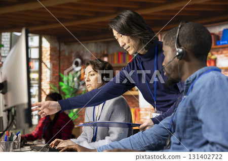 Asian call center manager providing guidance to multiethnic team, addressing questions. Customer support workplace onboarding specialist conducting orientation session for multiracial colleagues 131402722