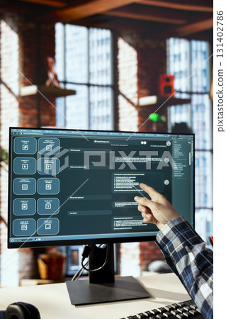 Worker in home office uses AI LLM chatbots designed to understand human language. Man in apartment workspace pointing finger to AI chatbot trained on data enabling them to perform complex tasks 131402786