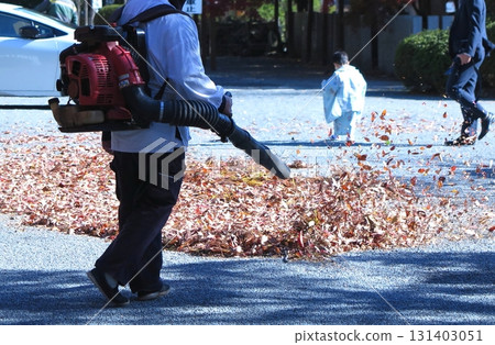 A shrine parking lot worker (chest down) uses a backpack blower to collect dead leaves. A shrine parking lot worker (chest down) uses a backpack blower to collect dead leaves. 131403051