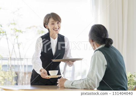 一位中年女工作人員正在為一位老人倒茶 131404040