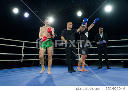 Boxing referee declares victorious fighter amidst the aftermath of an intense bout. 131404044