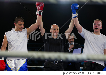 Boxing referee declares victorious fighter amidst the aftermath of an intense bout. Boxing referee declares victorious fighter amidst the aftermath of an intense bout. 131404049