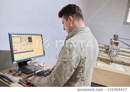 Operator Entering Coordinates on Computer for CNC Machine to Precisely Cut Wooden Pieces 131404417