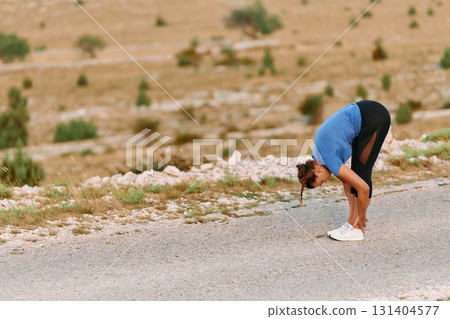 Determined Female Athlete Stretching After an Intense Run Through Rugged Mountain Terrain. 131404577