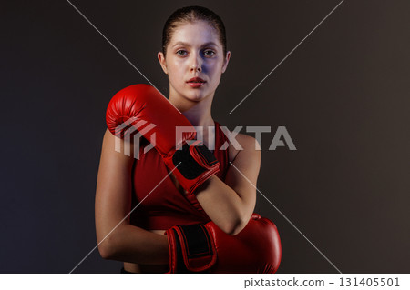 Confident young female boxer with red gloves posing in studio, athletic strength, focus and fitness training Confident young female boxer with red gloves posing in studio, athletic strength, focus and fitness training 131405501
