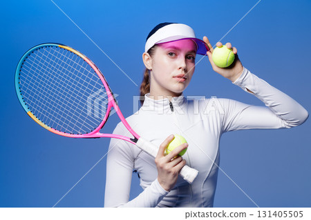 Confident woman tennis player holding racket and balls in studio on blue background wearing visor and sportswear Confident woman tennis player holding racket and balls in studio on blue background wearing visor and sportswear 131405505