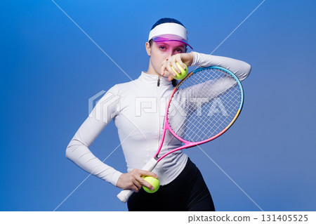 Confident tennis player holds racket and balls in studio on blue background, ready for training and competition Confident tennis player holds racket and balls in studio on blue background, ready for training and competition 131405525