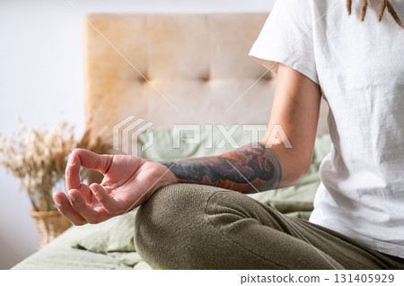 Woman meditating in lotus position with tattoo on arm. 131405929