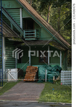 Old wooden house with green walls and stacked timber boards covered by a tarp in front Old wooden house with green walls and stacked timber boards covered by a tarp in front 131406476