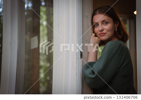 Woman in a green dress leans against a doorway, gazing softly at the camera with natural expression and warm light Woman in a green dress leans against a doorway, gazing softly at the camera with natural expression and warm light 131406706