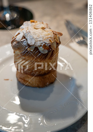 Golden almond cruffin topped with powdered sugar and sliced almonds, served on an elegant white plate 131406862