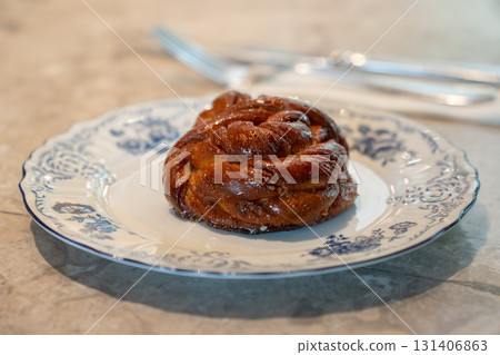 Freshly baked cinnamon bun with glossy caramelized crust served on a vintage blue-and-white porcelain plate 131406863