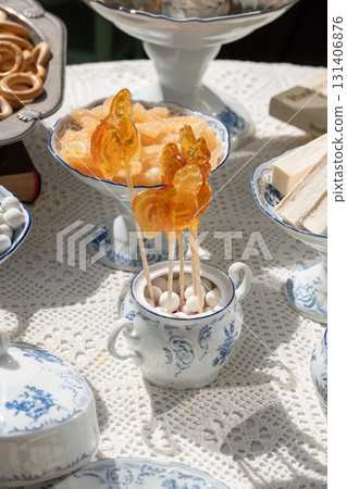 Traditional Russian sweets including rooster lollipops, baranki, zephyr, and candied fruits served in vintage porcelain and silverware under sunlight 131406876