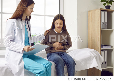 Child girl sitting in the doctor's office pointing to her stomach during medical exam in clinic. Child girl sitting in the doctor's office pointing to her stomach during medical exam in clinic. 131407287
