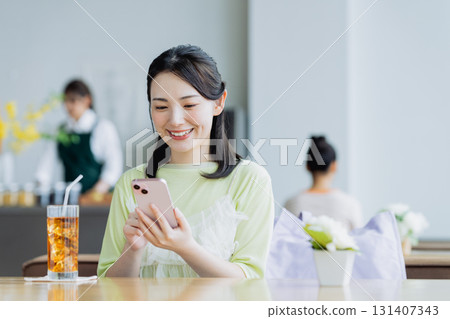 一個年輕的女人，看著一家咖啡館的智能手機 131407343