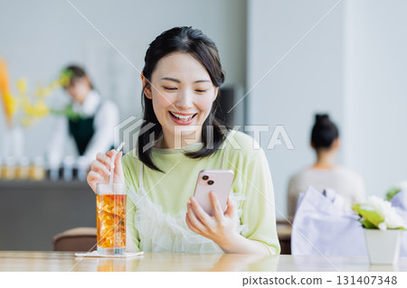 一個年輕的女人,看著一家咖啡館的智能手機 一個年輕的女人,看著一家咖啡館的智能手機 131407348