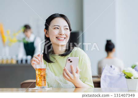 一個年輕的女人，看著一家咖啡館的智能手機 131407349