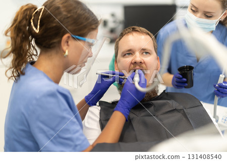 Two women dentists treating a man teeth 131408540