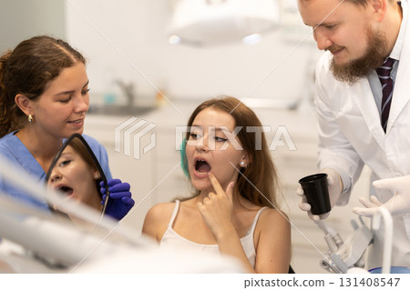 woman at a dentist appointment holds a mirror and looks at the tooth 131408547
