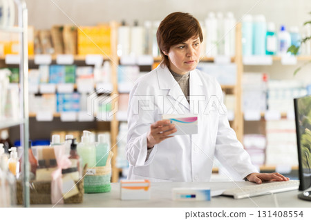 Female pharmacist checking stock of medicines, offering to customer at pharmacy 131408554