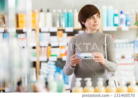 Woman in autumn clothes buys medicinal ointment at pharmacy 131408570