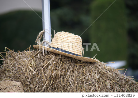 A straw hat rests atop a haystack, with wheat stalks, capturing a rustic countryside scene. A straw hat rests atop a haystack, with wheat stalks, capturing a rustic countryside scene. 131408829