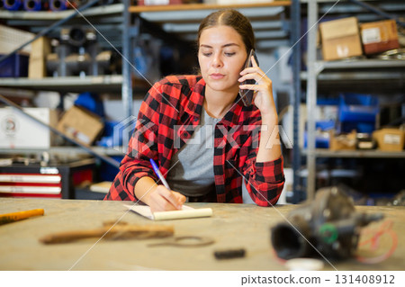 Young positive woman taking order at workplace talking mobile phone 131408912
