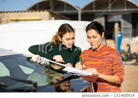 Asian woman farmer with female partner signing documents near car Asian woman farmer with female partner signing documents near car 131408914