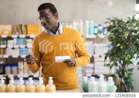 Man in glasses attentively carefully selects pills in modern pharmacy 131408916