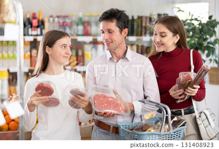 Dad, mom and daughter choose raw meat product and dry sausage in shop 131408923