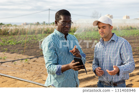 Aafrican american agronomist with phone talking to farmer at field Aafrican american agronomist with phone talking to farmer at field 131408946