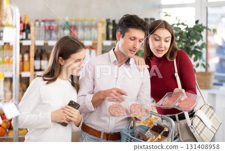 Dad, mom and daughter choose raw cooled semi-finished hamburger cutlet in shop Dad, mom and daughter choose raw cooled semi-finished hamburger cutlet in shop 131408958